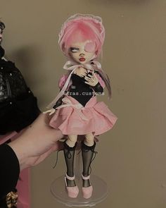 a hand holding a doll with pink hair and black stockings on it's feet