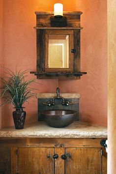 a bathroom sink sitting under a mirror next to a potted plant and wooden cabinet