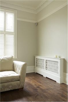 a white couch sitting next to a window with shutters on both sides and a rug on the floor in front of it