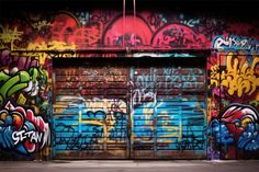 two garage doors covered in colorful graffiti on the side of a building with closed shutters