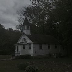 an old white church with a steeple and clock tower in the middle of trees