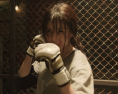 a young woman wearing boxing gloves standing in front of a fence