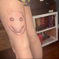 a woman's leg with a smiley face tattoo on it and a bookcase in the background