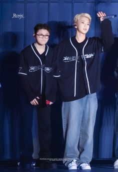 two young men standing next to each other in front of a blue wall with writing on it