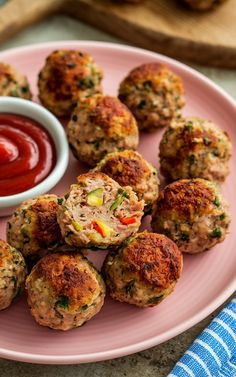 a pink plate topped with meatballs and ketchup next to a bowl of dipping sauce