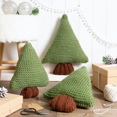 three knitted christmas trees sitting on the floor next to boxes, scissors and other items