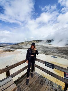 a woman standing on top of a wooden deck next to a geyser field