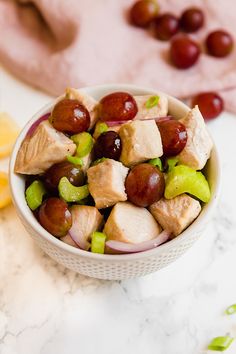 a bowl filled with grapes and chicken on top of a marble counter next to sliced lemons