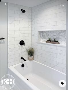 a bathroom with white tile and black fixtures in the bathtub, along with a potted succulent plant