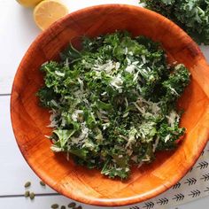 a wooden bowl filled with green vegetables on top of a white table next to sliced lemons