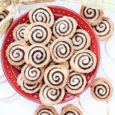 a red bowl filled with cinnamon rolls on top of a white table next to ribbon