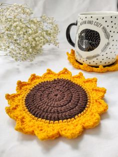 two crocheted coasters sitting on top of a table next to a coffee cup