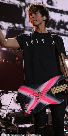 a young man holding a guitar while standing on top of a stage with other instruments