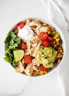 a white bowl filled with chicken, rice and avocado on top of a table