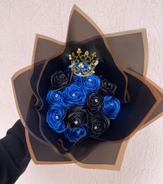 a paper flower bouquet with blue roses and a crown on top is held by someone's hand