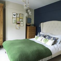 a bedroom with a green blanket on the bed and dressers in the room behind it