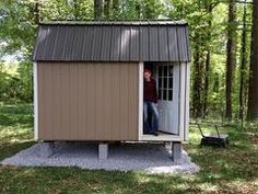 a man standing in the doorway of a small shed next to some trees and grass