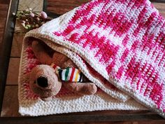 a crocheted blanket with a teddy bear under it on top of a wooden floor