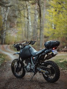 a motorcycle parked on the side of a dirt road next to a wooded area with lots of trees