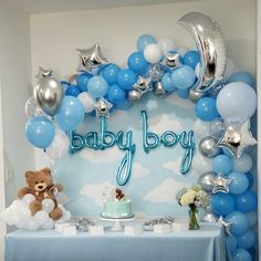 a blue and silver baby shower with balloons, teddy bear, cake and other items