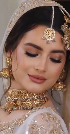 a woman wearing a gold and white bridal outfit with jewelry on her head, looking at the camera