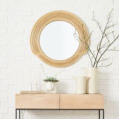 a white brick wall with a round mirror and vases on the table next to it