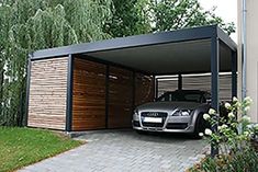 a car is parked in the garage next to some flowers and trees on the side of the road