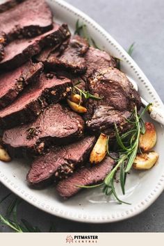 a white plate topped with sliced up steak and garnished with green herbs on top