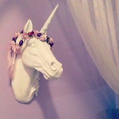 a white unicorn head mounted to the side of a wall with flowers on it's forehead