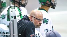 a man with glasses and a bald head is standing in front of some hockey players