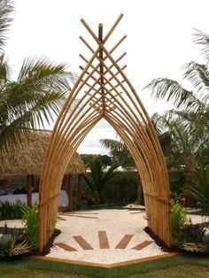 an arch made out of bamboo sticks and stones in the middle of a garden with palm trees