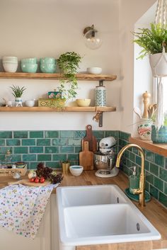 a kitchen with green tiles and wooden shelves on the wall above the sink is filled with dishes