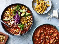 two bowls filled with chili, corn and avocado on top of a table