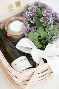 a white basket filled with bottles of wine and lavenders next to a bottle of wine