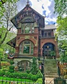 an old victorian house with many windows and steps leading up to the front door, surrounded by lush greenery