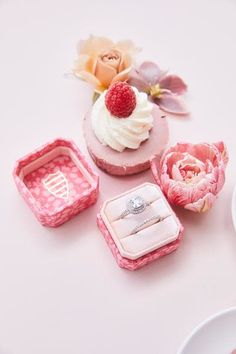 three miniature wedding rings and one ring box on a white table with flowers in the background