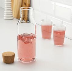 three glasses and a pitcher on a counter with pink liquid in the bottom, next to a cork stopper