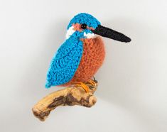 a small crocheted bird sitting on top of a tree branch next to a white wall