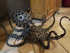 an octopus sculpture made out of metal gears on the floor in front of a cabinet