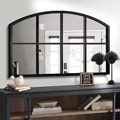 a large mirror on the wall above a console table with books and other items in front of it