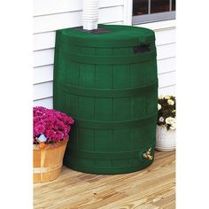 a large green water tank sitting on top of a wooden floor next to flowers and potted plants