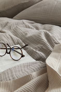 a pair of glasses sitting on top of a white bed cover covered in linens