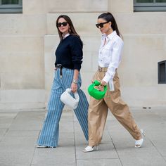 two women are walking down the street with handbags in their hands and one is carrying a green purse