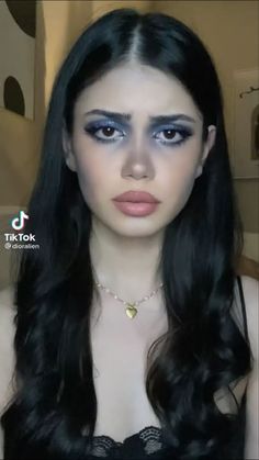 a woman with long black hair and blue makeup looks at the camera while wearing a choker