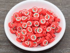 a white bowl filled with lots of red and green fruit shaped beads on top of a wooden table