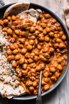 a bowl filled with chickpeas and rice on top of a wooden table next to a fork