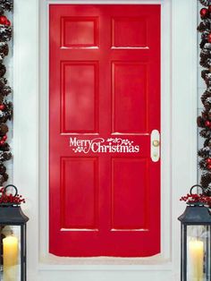 a red door with merry christmas lettering on it and two lanterns in front of it