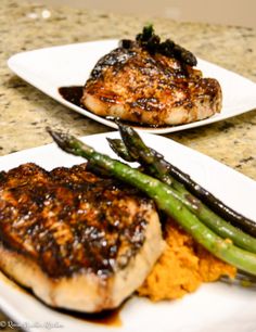 two white plates topped with meat and asparagus on top of a marble counter