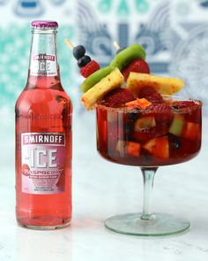 a glass filled with ice and fruit next to a bottle of smirnoff