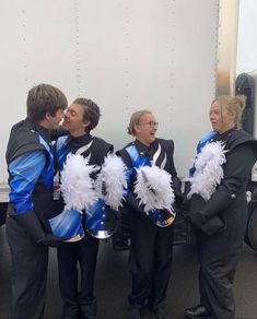 four people dressed in blue and white cheerleaders are standing next to a food truck